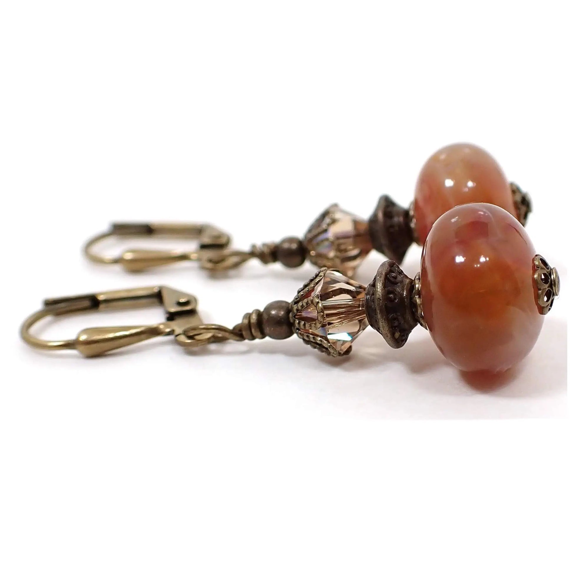 Side view of the handmade vintage lucite drop earrings. They have antiqued brass metal with faceted glass crystal beads at the top. The bottom lucite beads are rondelle shaped with marbled swirls of pink, orange, and white.