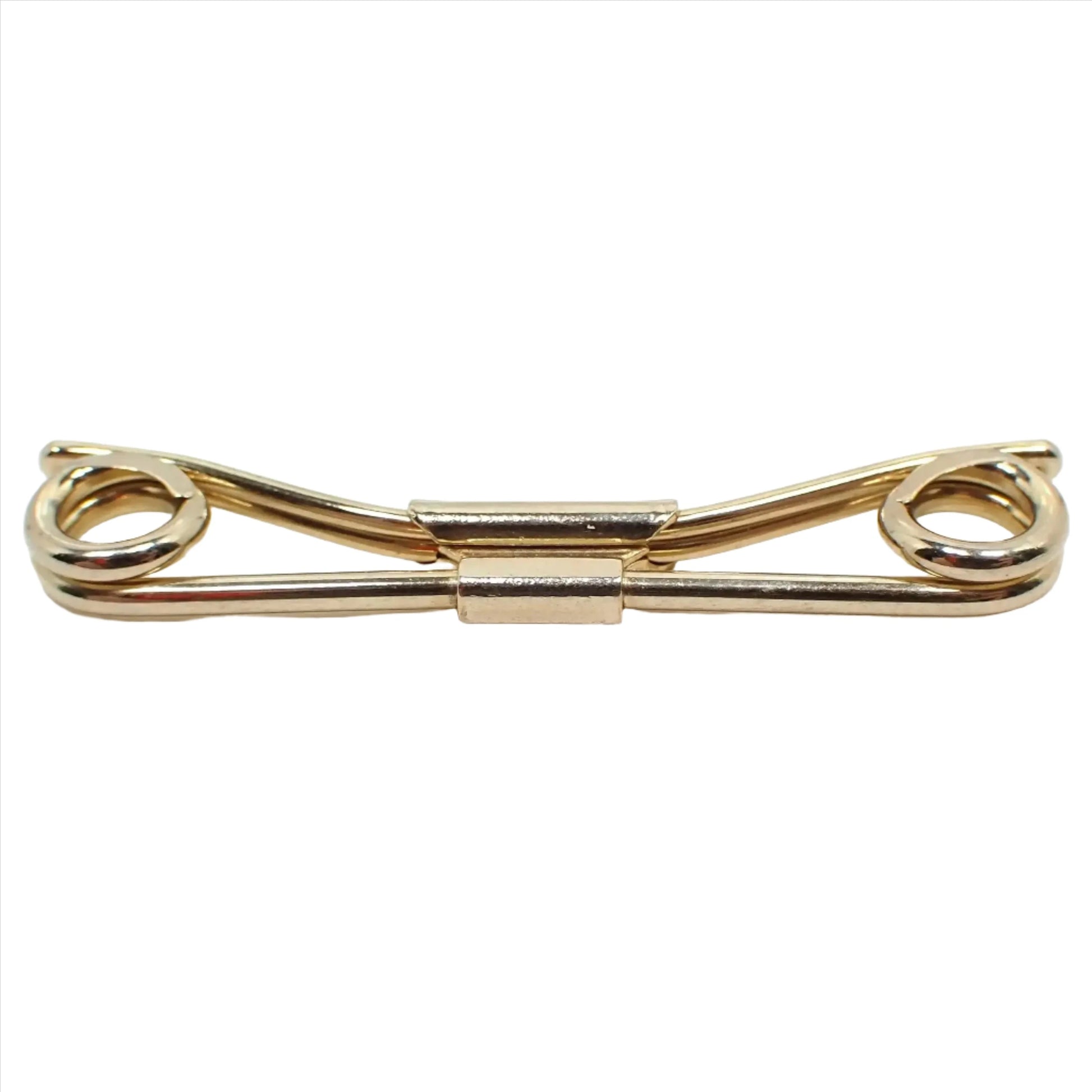 Enlarged front view of the Mid Century vintage Swank collar clip. It is gold tone plated in color. The front has a rounded bar that has spiral ends on each side. The back has a curved design with two thinner rounded bars together.