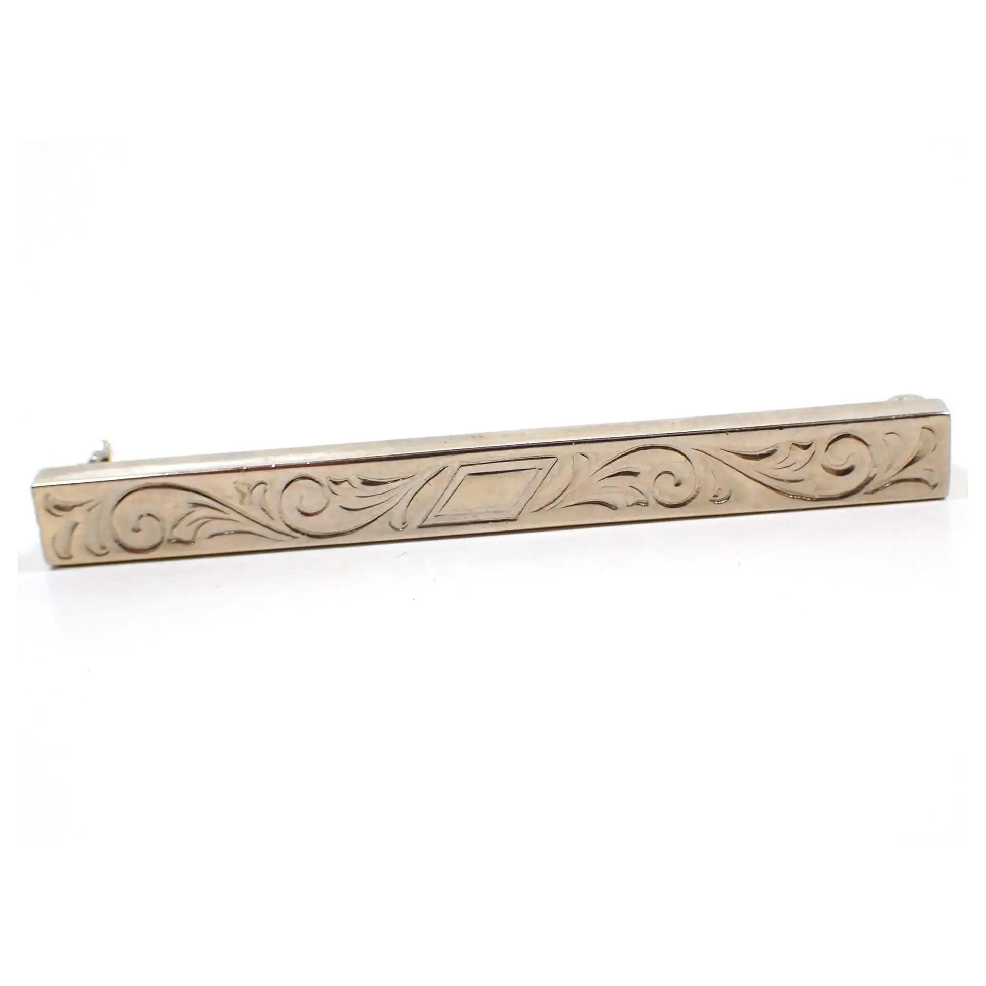 Enlarged front view of the Mid Century vintage bar brooch. It has a longer rectangle shape with an angled rectangle in the middle and scroll like leaf designs on either side. The metal is a slightly darkened silver tone color.