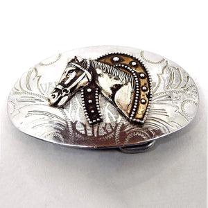 Front view of the retro vintage horse and horseshoe belt buckle. The buckle is oval and silver tone in color with an etched leaf like design. In the middle is a horse's head with a large horseshoe around its neck in an antiqued golden color.