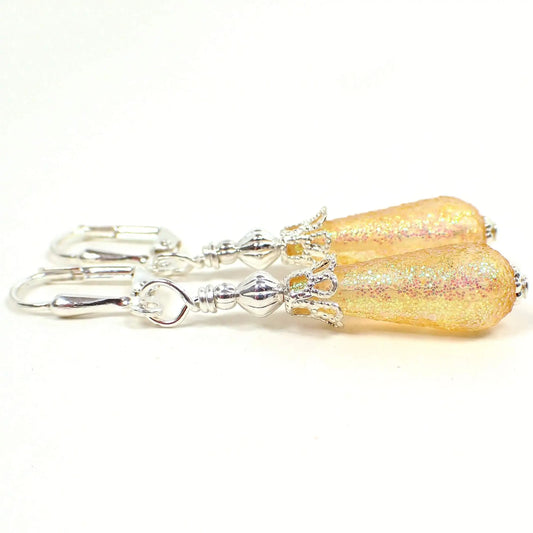 Side view of the small handmade glitter earrings with vintage lucite beads. The metal is silver plated in color. There are small yellow lucite teardrop beads on the bottom with glitter on the outside.
