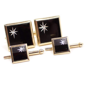 Front view of the Mid Century vintage Swank jewelry set. The metal is gold tone in color. There are squares on the fronts with half black and half metallic gray colors. On the metallic gray side is an etched starburst design. There are two shirt studs in the front and two cufflinks in the back on this photo.