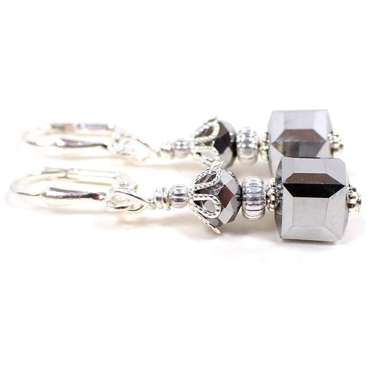 Side view of the handmade small cube earrings. The metal is silver plated in color. There are faceted metallic silvery gray glass rondelle beads at the top and square cube beads at the bottom.