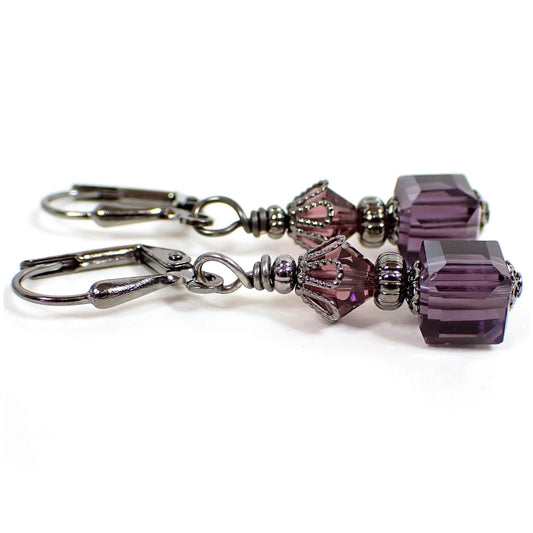 Side view of the handmade small cube drop earrings. The metal is gunmetal gray in color. There are purple faceted glass crystal bicone beads on the top and purple faceted glass crystal cube beads on the bottom.