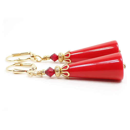 Side view of the handmade geometric cone earrings. The metal is gold plated in color. There is a faceted glass crystal bead at the top in dark red. The bottom bead is a vintage lucite cone shaped bead in a brighter red color.