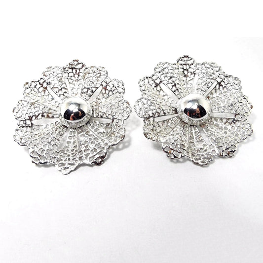 Front view of the Mid Century vintage Sarah Coventry clip on earrings. They are silver tone in color with a large filigree flower design.