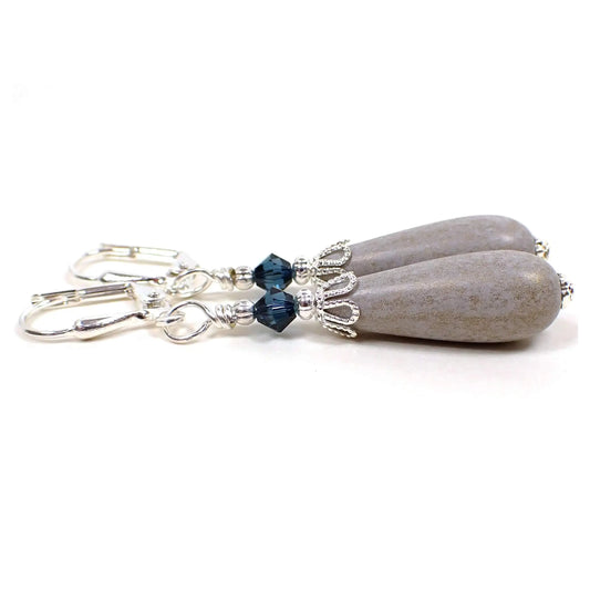Side view of the handmade earrings with vintage lucite beads. The metal is silver plated in color. There are dark blue faceted glass crystal beads at the top. The bottom vintage lucite beads are teardrop shaped and are a light gray color with light golden sheen on the outside.