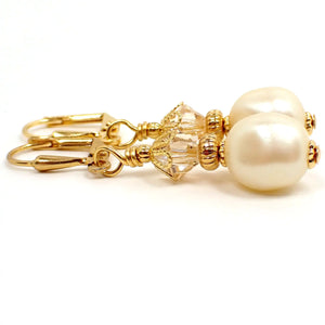 Side view of the handmade drop earrings with vintage lucite beads. The metal is gold plated in color and there are faceted glass crystals at the top. The bottom vintage beads are potato shaped with indents and are pearly off white like faux pearls.