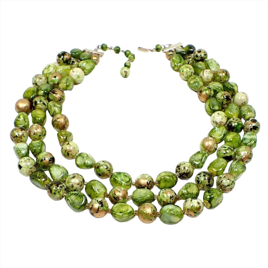 Top view of the Hong Kong Mid Century vintage multi strand beaded necklace. The beads are round and nugget style shaped. They are marbled with shades of mossy green and have a black and metallic gold paint splatter design on them. There is a gold color hook clasp at the end to adjust the size some.