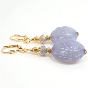 Side view of the handmade oval drop earrings with raised floral design. The metal is gold plated in color. There are new faceted glass beads in a light periwinkle color at the top of the earrings. The bottom oval beads are vintage lucite with a raised leaf like flower design and are a light periwinkle purple in color as well. Depending on the lighting the beads may take on more of a bluish hue.