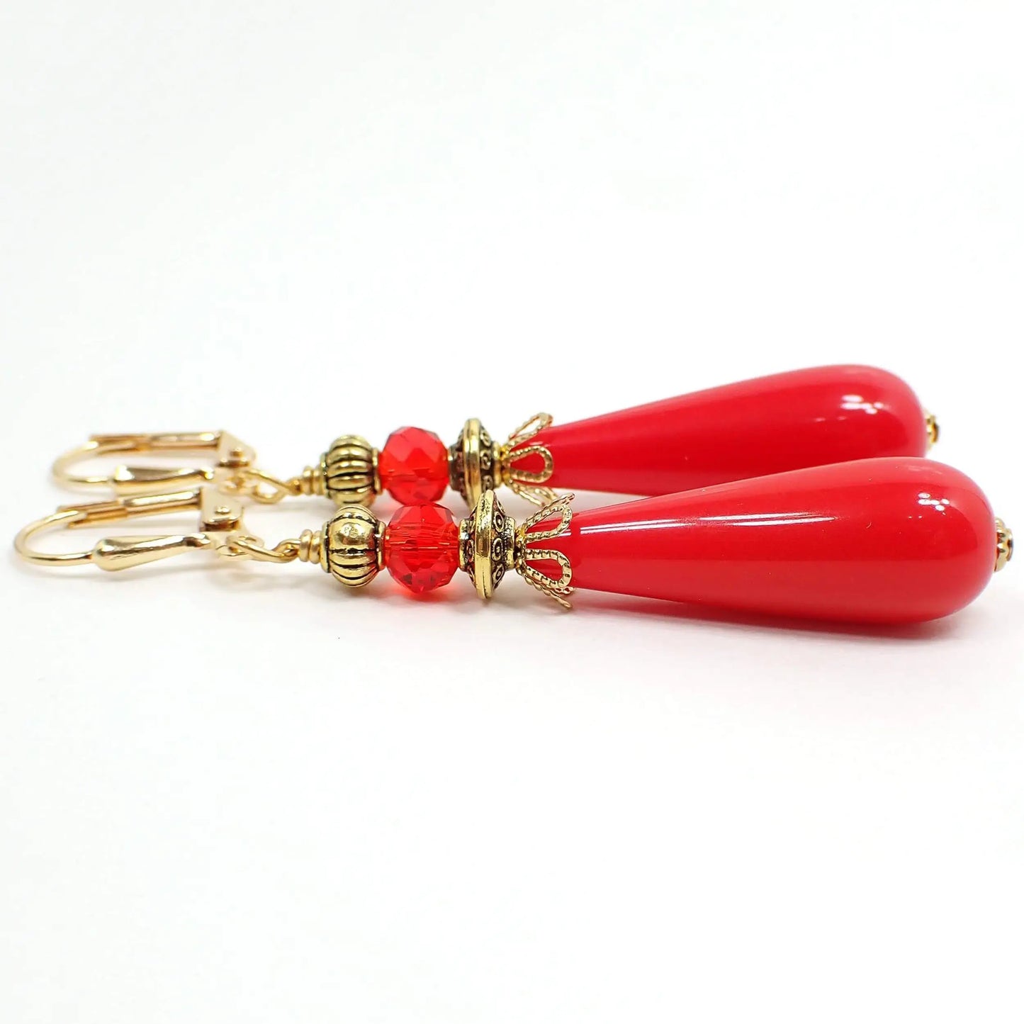 Side view of the handmade teardrop earrings. The metal is gold plated in color. There are faceted red color glass crystal beads at the top. The bottom teardrop beads are bright red vintage lucite beads.