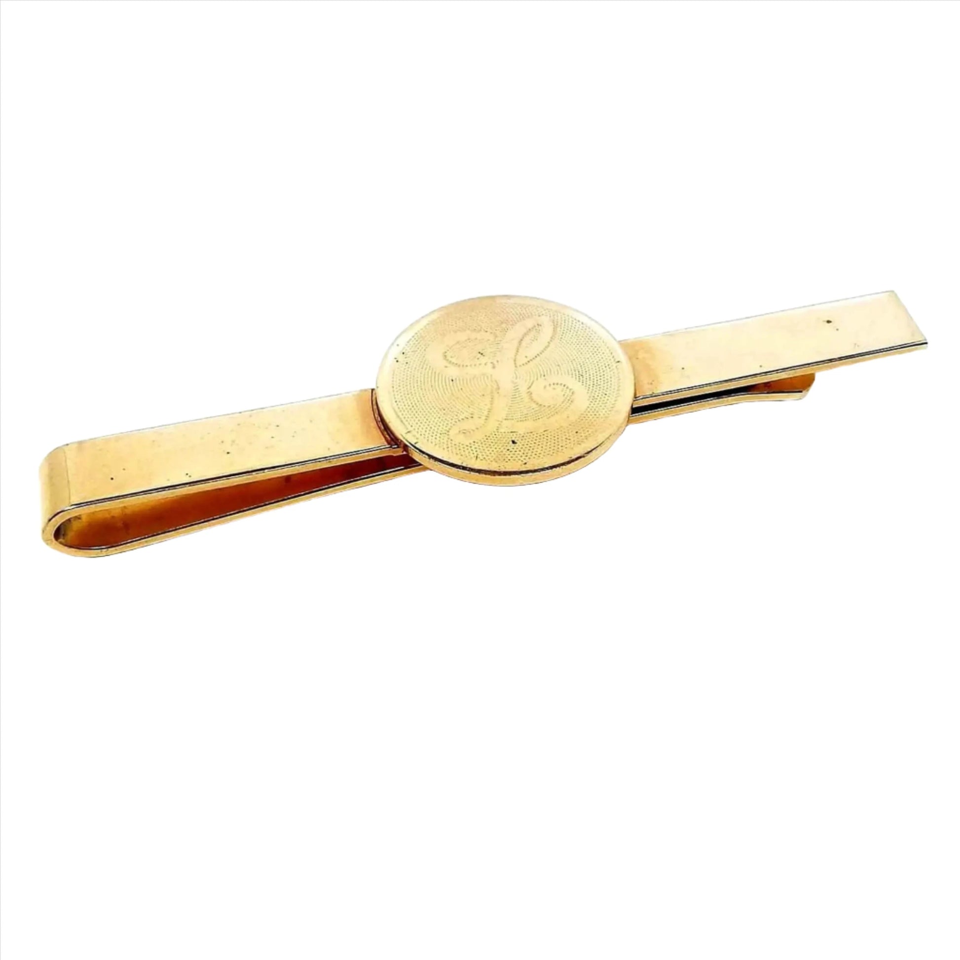 Front view of the retro vintage slide on initial tie bar. It is gold tone in color. There is a circle in the middle with a light texture on it and a script letter L.