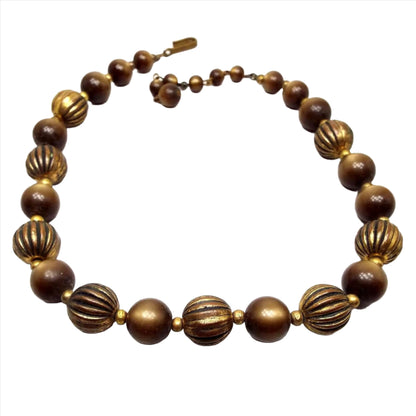 Top view of the Mid Century vintage moonglow lucite and antiqued brass necklace. The beads are round in shape. The brass beads are dark brass in color and are corrugated with lines. The moonglow lucite beads are a golden brown in color and the hues shift with a glowy appearance as you move around. There is a hook clasp at the end.