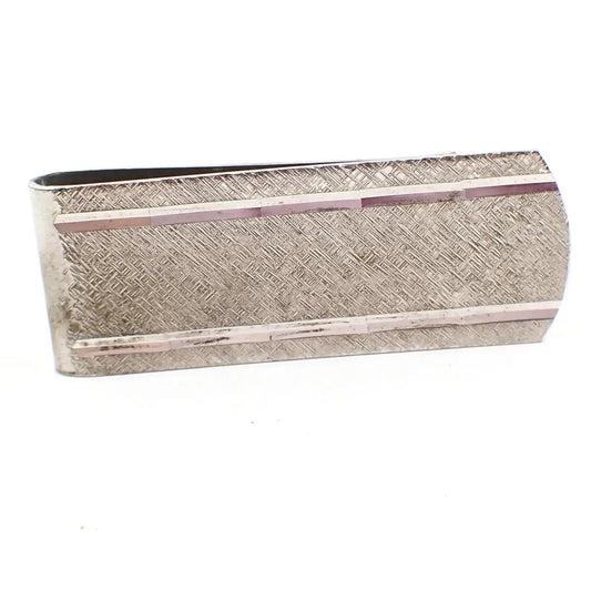 Angled front view of the Mid Century vintage sterling silver money clip by Simmons. The front is rectangular shaped with a curved end. It has a brushed matte design on the front with diamond cut edge lines at the top and bottom.