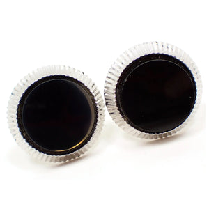 Enlarged front view of the retro vintage Hickok Cufflinks. They are silver tone plated in color and have a round shape. There is a corrugated textured edge and a flat round black glass cab in the middle.