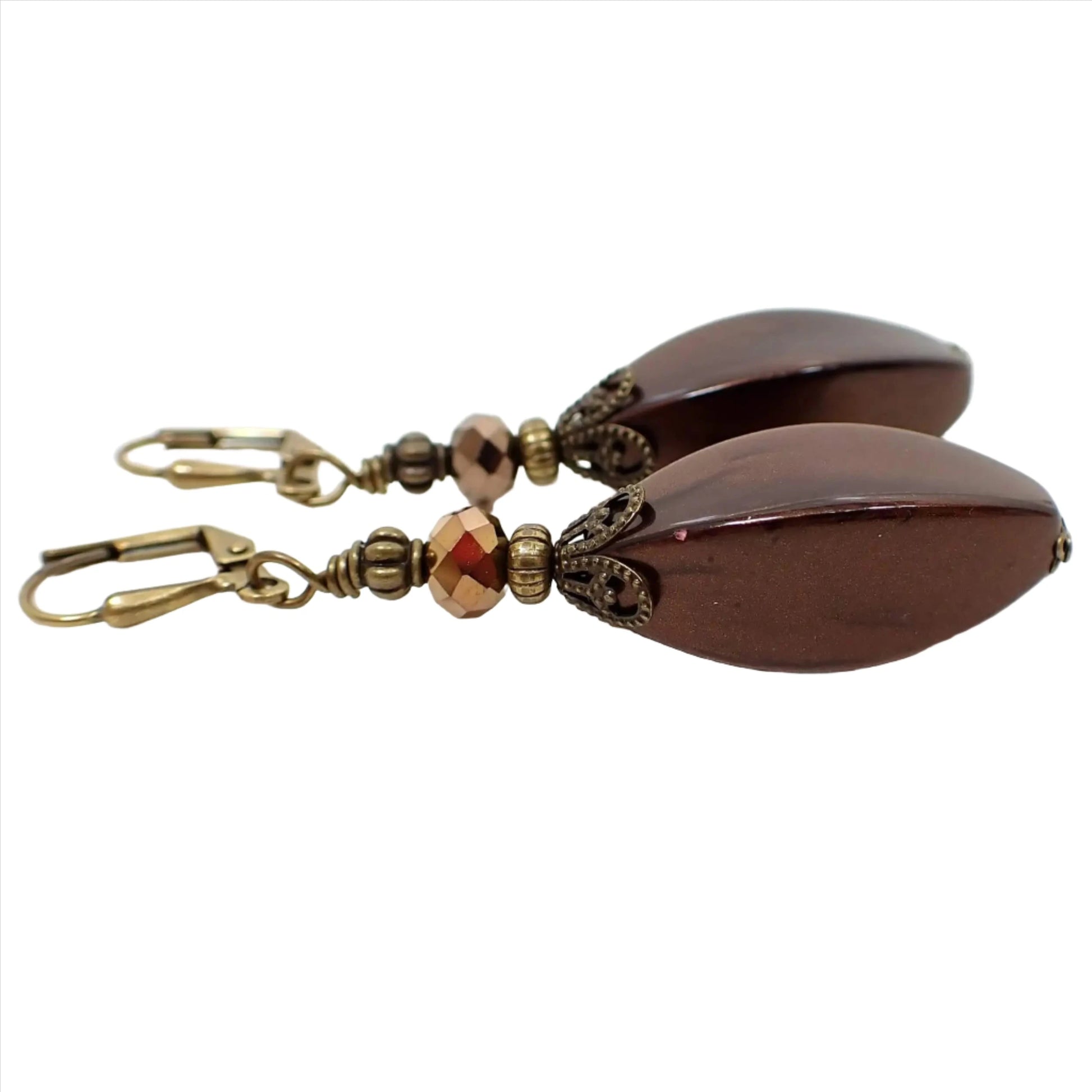 Side view of the handmade large brown drop earrings. The metal is antiqued brass in color. There are large vintage lucite beads at the bottom in pearly dark mocha brown color. The top glass crystal beads are faceted and metallic bronze in color.