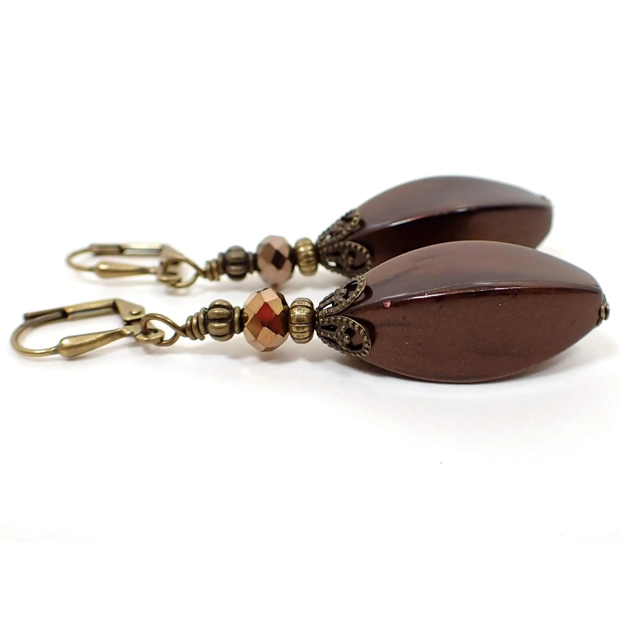 Side view of the handmade large brown drop earrings. The metal is antiqued brass in color. There are large vintage lucite beads at the bottom in pearly dark mocha brown color. The top glass crystal beads are faceted and metallic bronze in color.