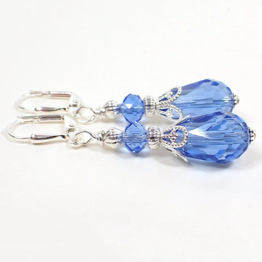 Side view of the handmade teardrop earrings. The metal is silver plated in color. There are faceted glass crystal rondelle beads at the top and teardrop beads at the bottom. The beads are a light blue in color.