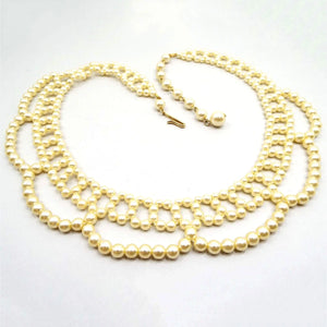 Top view of the retro vintage faux pearl collar bib necklace. The necklace is beaded to look like a collar with open areas at the bottom edge. The plastic imitation pearls are off white yellow golden in color and there is a gold tone color hook clasp at the end.
