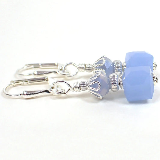 Side view of the small handmade cube earrings. The metal is silver plated in color. There are light opaque blue faceted glass rondelle beads at the top and small square cube beads at the bottom.