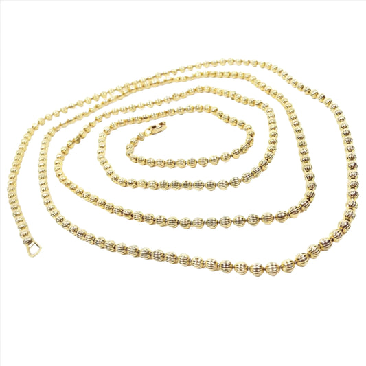 Top view of the Mid Century vintage Coro long beaded necklace. The necklace has gold tone color corrugated round beads all the way down. It has a snap lock clasp on the end.