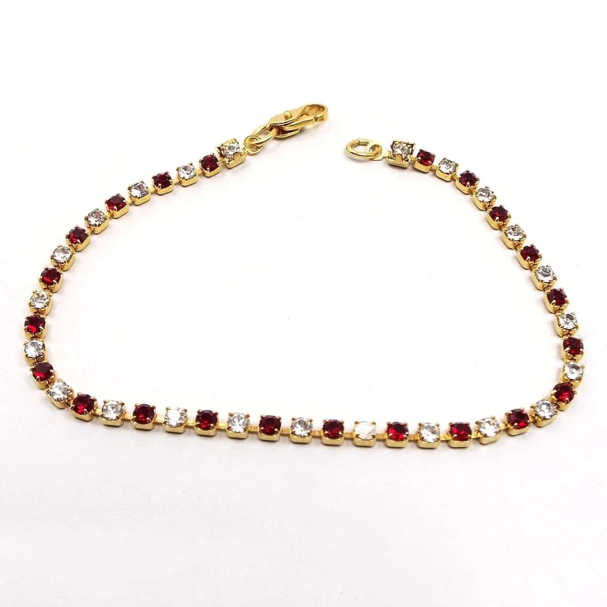 Top view of the retro vintage rhinestone bracelet. The metal is gold tone in color. There are small round rhinestones alternating in color between red and clear. There is a lobster claw clasp at the end.