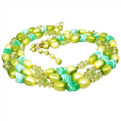 The Mid Century vintage beaded multi strand necklace from Hong Kong. It has three strands of plastic beads in varying shades of bright to medium green. It has a fairly chunky appearance with disc, saucer, nugget, and round shaped beads.