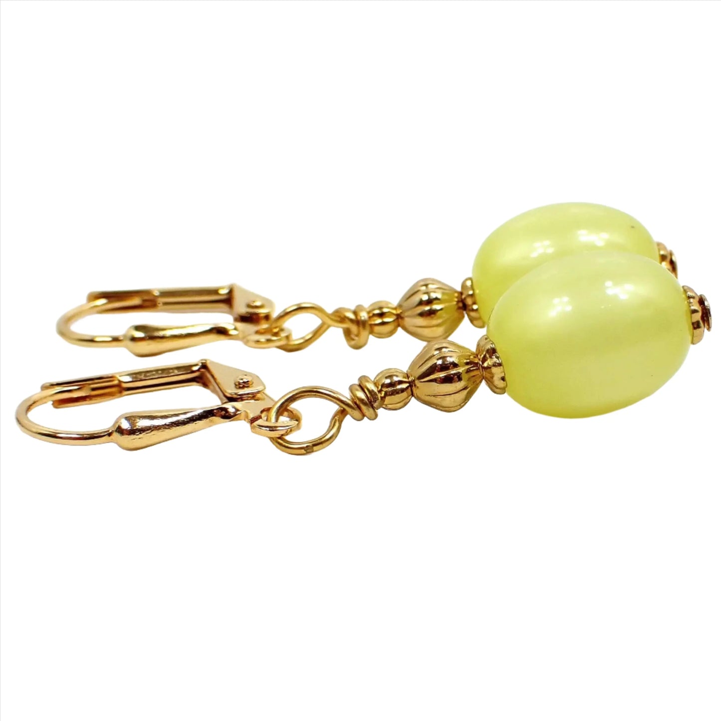 Side view of the handmade drop earrings with vintage lucite beads. The metal is gold plated in color. There is an oval moonglow lucite bead at the bottom in a citrusy yellow color that has a hint of green to it.