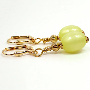 Side view of the handmade drop earrings with vintage lucite beads. The metal is gold plated in color. There is an oval moonglow lucite bead at the bottom in a citrusy yellow color that has a hint of green to it.