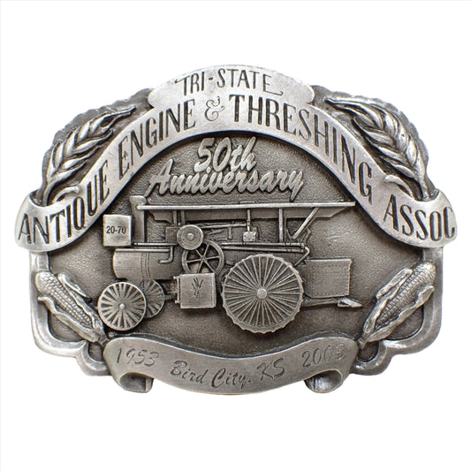 Front view of the pre owned modern Antique Engine and Threshing Association belt buckle. It's made of pewter and a gray in color. The association's name is at the top and then it shows 50th anniversary and 1953 Bird City, KS 2003. There is an old piece of farm equipment depicted in the middle with corn and wheat at the corners.