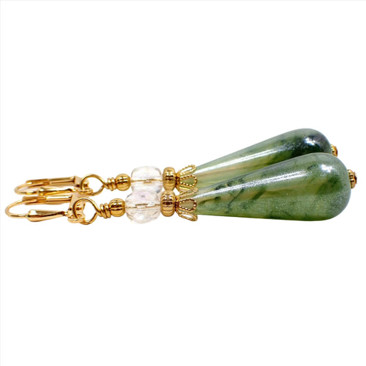 Side view of the handmade teardrop earrings. The metal is gold plated in color. There is a faceted oval AB clear glass crystal bead at the top. The bottom teardrop bead is a vintage lucite bead with marbled swirls in shades of green.