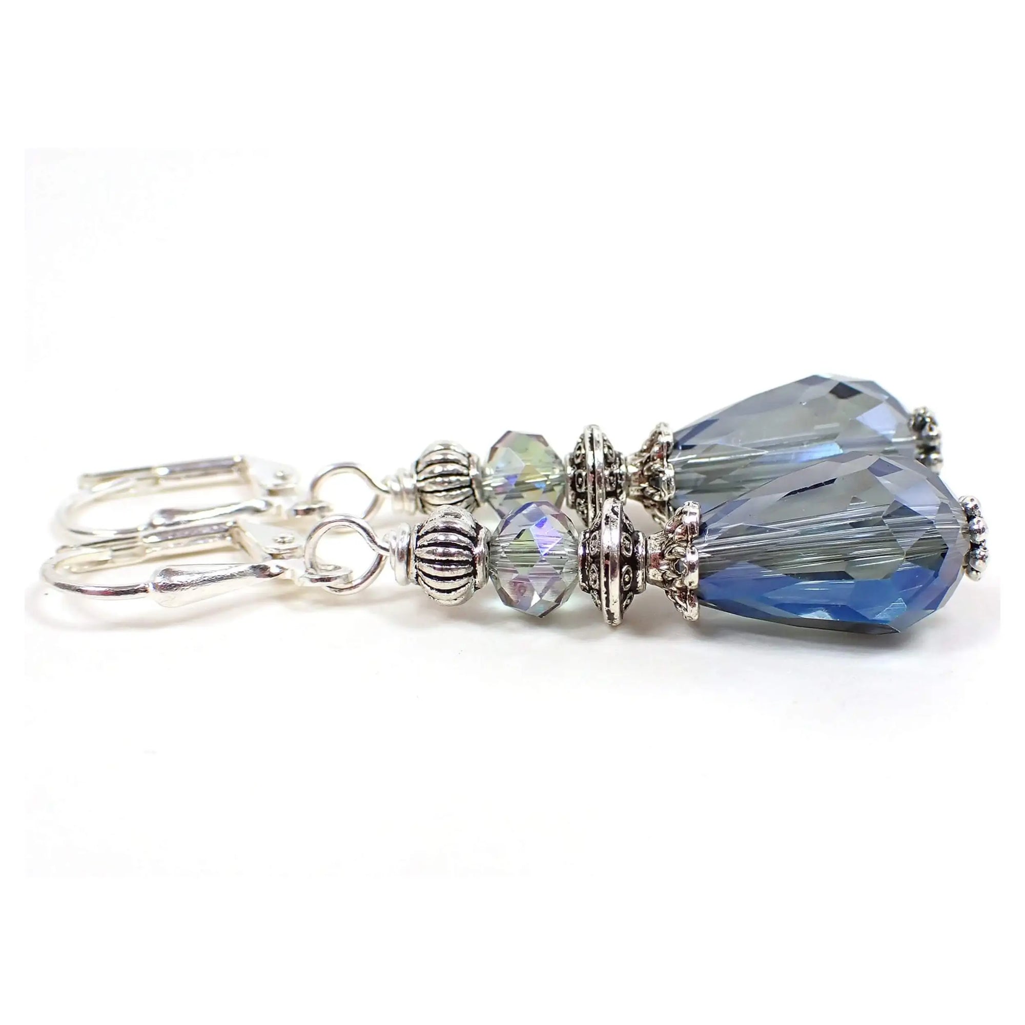 Side view of the handmade teardrop earrings. The metal is silver plated in color. There are AB smoky blue faceted glass crystal rondelle beads at the top and teardrop beads on the bottom.