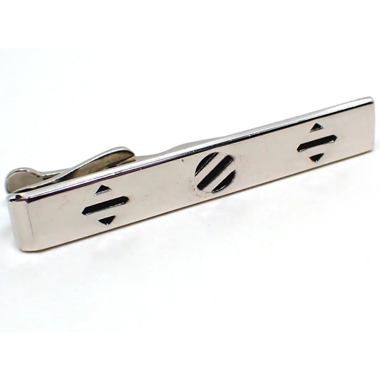 Angled front view of the retro vintage Swank tie clip. The metal is silver tone in color. It has a long rectangular shape. There is a pattern on the front with a diamond shape, a circle, and another diamond shape. Each shape is silver tone with black painted lines.