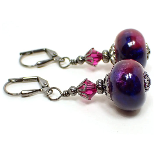 Side view of the beaded earrings with handmade resin beads. The metal is dark gunmetal gray in color. There are small faceted glass crystal bicone beads at the top in a bright fuchsia pink color. The resin beads are rondelle rounded saucer like shaped and have marbled shades of pearly bright pink and blue.