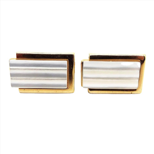Front view of the Mid Century vintage modernist Swank cufflinks. they have a rectangle design with gold tone color metal. There is a longer rectangle in the middle that extends past one side with pearly white carved mother of pearl shell cabs.