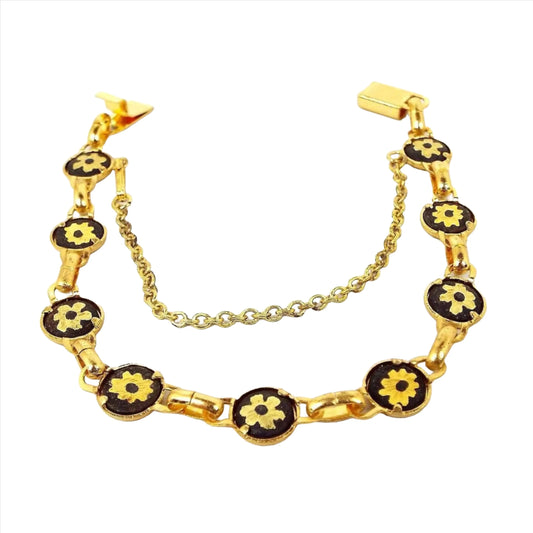 Front view of the retro vintage Damascene style bracelet. It is gold tone in color. The round links are painted black and have a gold tone flower design in the middle. There is a box clasp at the end and a safety chain with a hinged clip clasp as well.