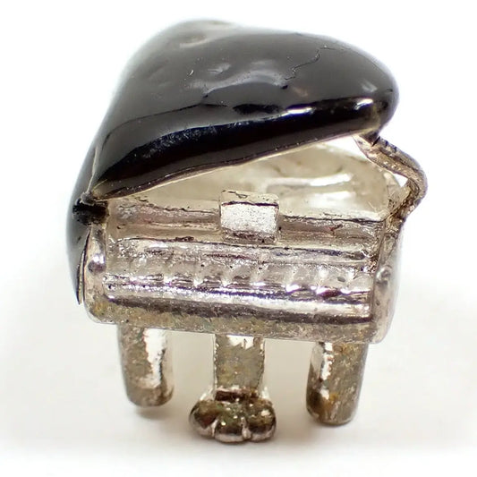 Enlarged front view of the small retro vintage piano charm. It is sterling silver and shaped like a grand piano. the top of the piano is black enameled. 
