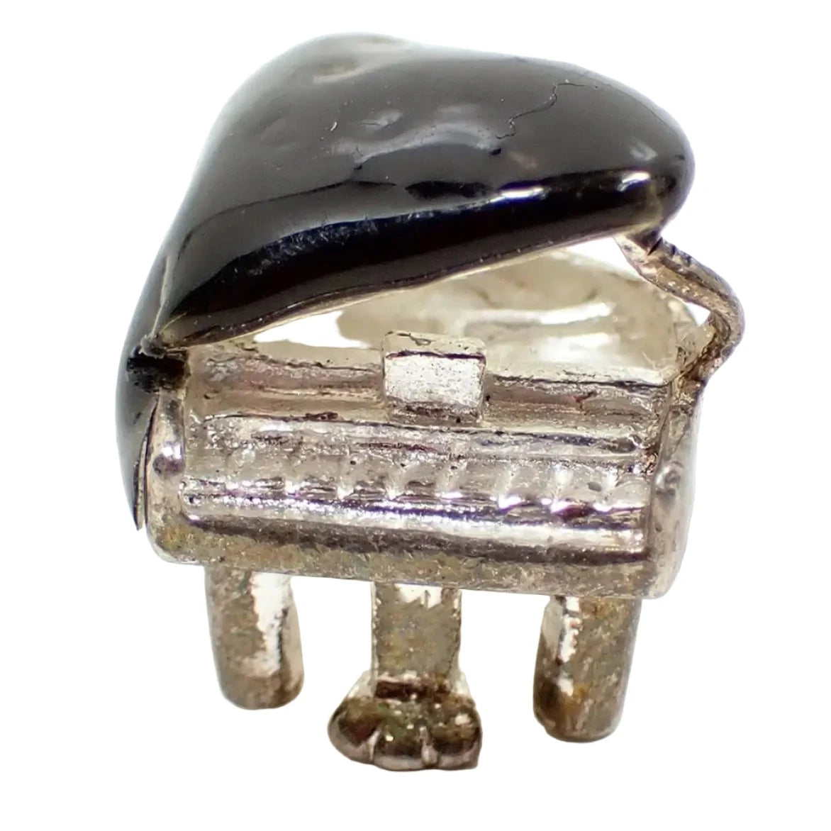 Enlarged front view of the small retro vintage piano charm. It is sterling silver and shaped like a grand piano. the top of the piano is black enameled. 
