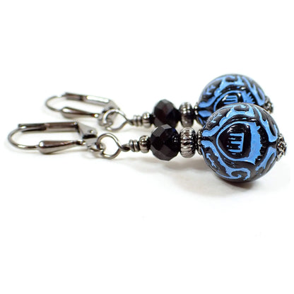 Side view of the handmade drop earrings. The metal is gunmetal gray in color. There are black faceted glass beads at the top. The bottom acrylic beads are round and are blue and black and with a raised pattern on them.