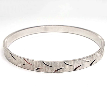 Angled side view of the Mid Century vintage Crown Trifari bangle bracelet. It is silver tone in color and has an etched thin line and curve pattern all the way around the outside of the bracelet.