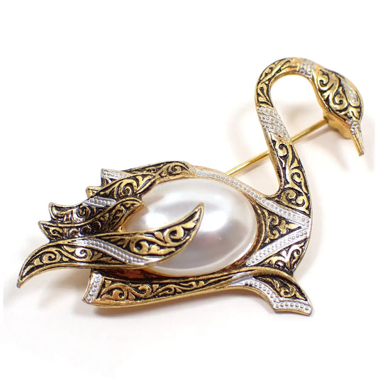 Enlarged view of the Mid Century vintage Damascene brooch from Spain. It is shaped like the side view of a swan. The metal is mainly gold tone in color with black and silver color pattern. The swan body is a large plastic imitation pearl.