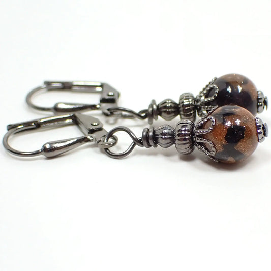 Photo of the handmade goldstone drop earrings. They have gunmetal gray color beads and findings. There are small round ball goldstone beads at the bottom. The goldstone beads are marbled with orange glass that has tiny flecks of copper and black.