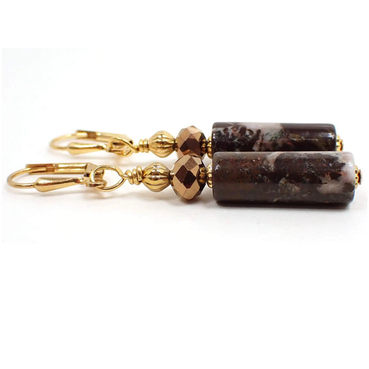 Side view of the handmade portoro marble earrings. The metal is gold plated in color. There are faceted metallic bronze color glass beads at the top and tube shaped gemstone beads at the bottom. The marble beads have shades of brown and cream color.