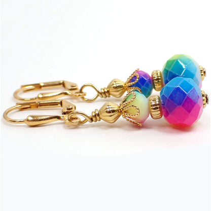 Side view of the rainbow earrings. The metal is gold plated in color. There are faceted glass rondelle beads at the top and larger ones at the bottom. They have different vibrant colors of the rainbow blended all the way around the beads.