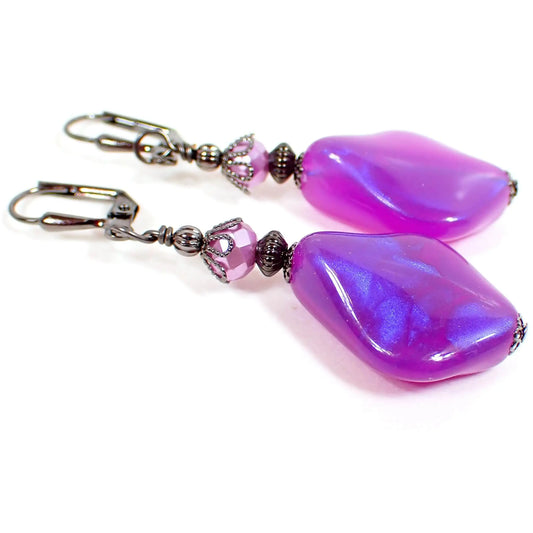 Front view of the handmade color shift purple lucite earrings. The metal is dark gray gunmetal plated in color. There are pearly glass faceted beads at the top and angled teardrop beads at the bottom. The bottom beads have an indented curve and are a bright purple in color with hints of another shade of sparkly purple as you move around.