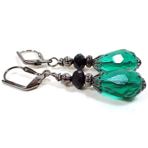 Side view of the handmade teardrop earrings. The metal is gunmetal gray in color. There are faceted black beads at the top. The bottom crystal glass beads are faceted teardrop shaped and are a teal green in color.