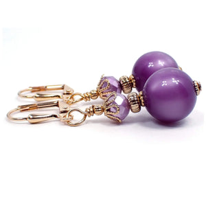 Side view of the handmade lucite drop earrings. The metal is gold plated in color. There are faceted light purple glass beads at the top. The bottom beads are round moonglow lucite beads in a lilac purple color. The lucite beads have a glowy effect as you move around in the light.