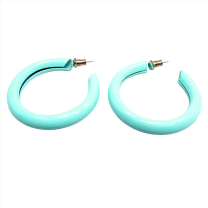 Angled side view of the retro vintage enameled hoop earrings. They are mostly sea foam blue green in color and have post ends with earring clutches attached.