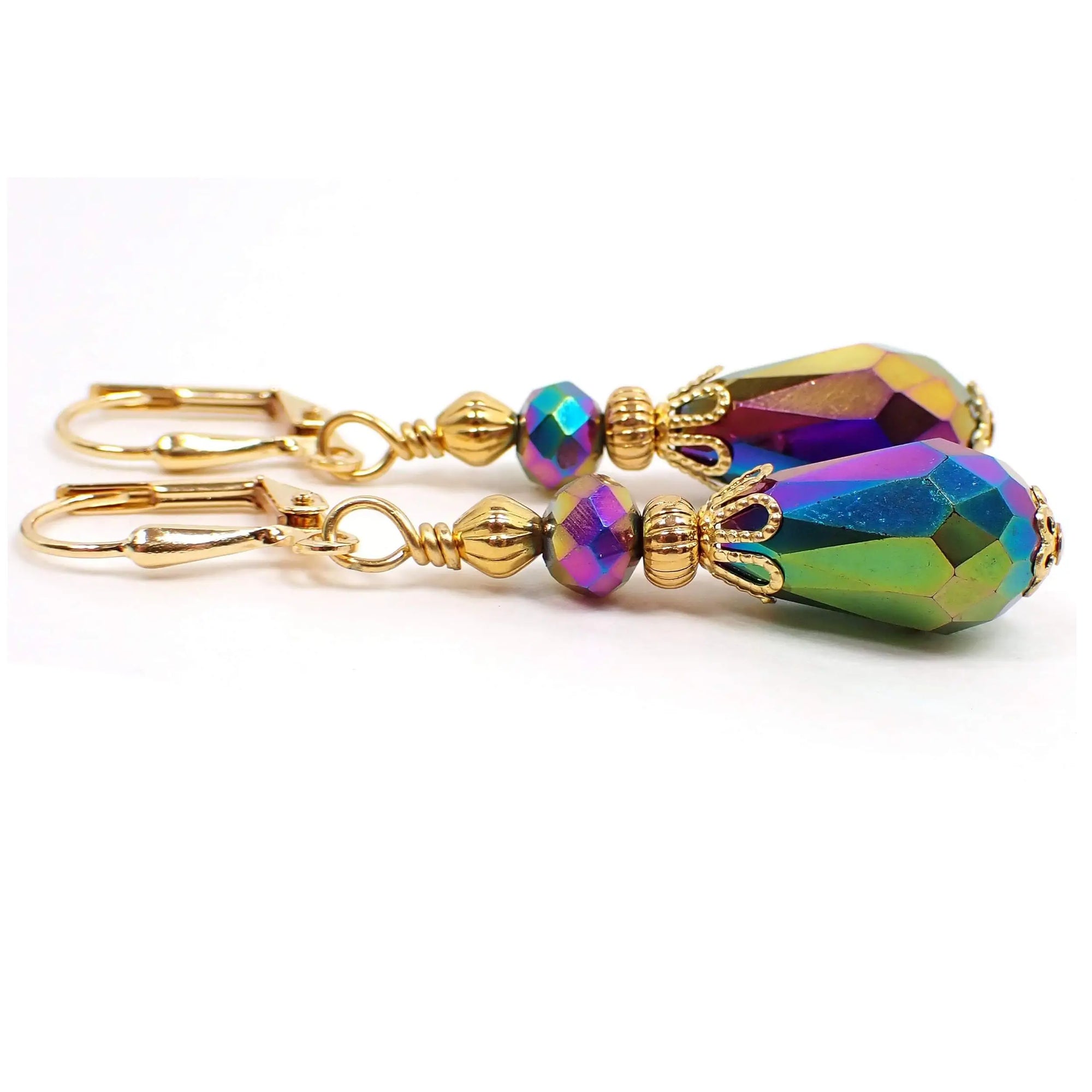 Side view of the handmade rainbow metallic multi color earrings. They have saucer shaped faceted glass beads at the top and faceted glass teardrop beads at the bottom. They colors are different as you rotate around the beads in pink, blue, purple, and yellow. The metal is gold plated color.