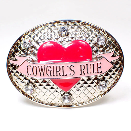 Front view of the pre owned Nocona belt buckle. It is silver tone plated in color and is an oval shape with a textured raised quilted design. There is a bright pink enameled heart in the middle with a light pink banner across it that says "Cowgirl's Rule." There are round clear rhinestones around the top and the bottom of the belt buckle.